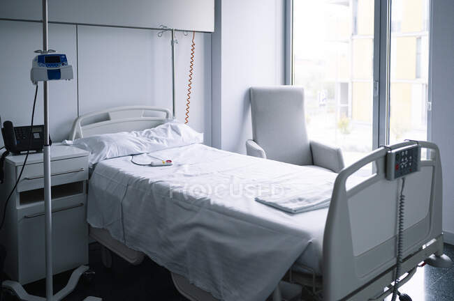 Порожнє ліжко з кнопкою виклику медсестри біля IV стійте у світлі, обладнаних у сучасній лікарні. — стокове фото