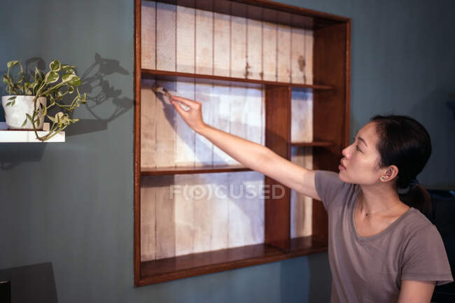 Seitenansicht der ethnischen Frau mit Pinsel Malerei Holzregale in weißer Farbe bei der Renovierung von Möbeln — Stockfoto