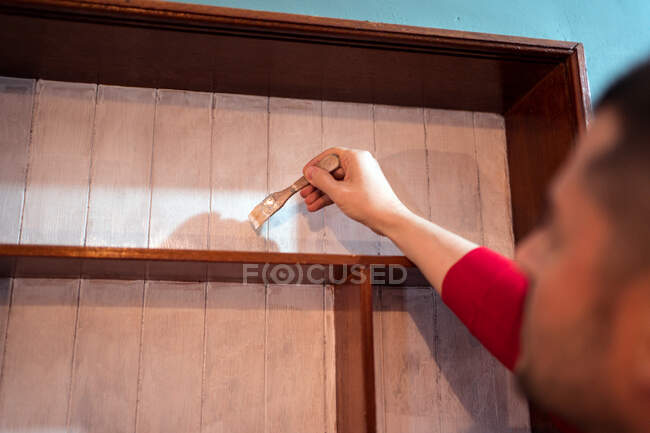 Vista laterale maschio con pennello pittura mensole in legno di colore bianco durante la ristrutturazione di mobili — Foto stock