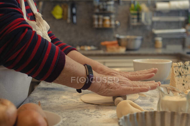 From above of crop unrecognizable elderly cook rolling out crust on table with flour while cooking in kitchen at home — Stock Photo