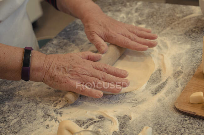 From above of crop unrecognizable elderly cook rolling out crust on table with flour while cooking in kitchen at home — Stock Photo