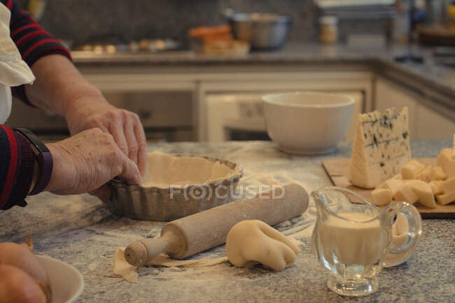 Crop anonymous chef with pastry crust above table with baking dish and assorted cheeses during cooking process — Stock Photo