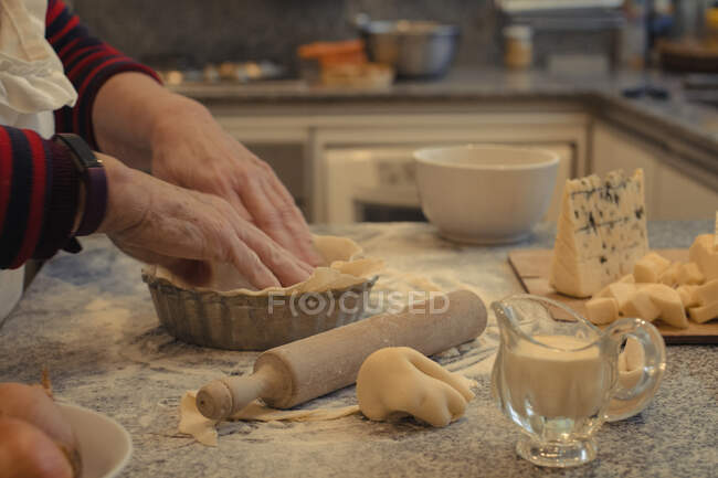 Crop anonymous chef with pastry crust above table with baking dish and assorted cheeses during cooking process — Stock Photo