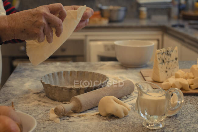 Crop chef anonimo con crosta pasticcera sopra la tavola con teglia e formaggi assortiti durante il processo di cottura — Foto stock