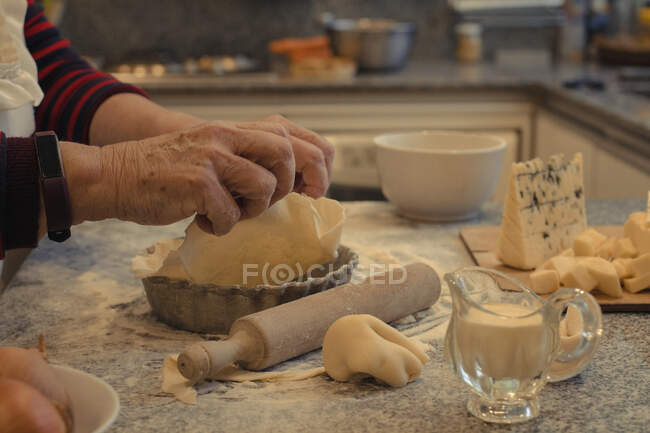 Crop chef anónimo con corteza de pastelería encima de la mesa con plato para hornear y quesos surtidos durante el proceso de cocción - foto de stock