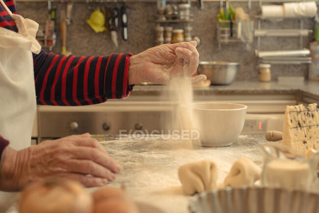 Side view of crop anonymous senior cook sprinkling table with flour after preparing pastry crust for quiche at home — Stock Photo