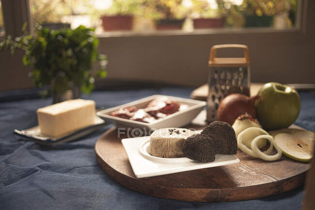 Trufas na placa perto de queijos e cebolas cruas com maçã na tábua de corte em casa — Fotografia de Stock