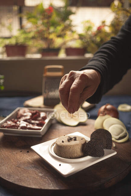 Анонимный повар урожая приправляет мягкий сыр трюфелем на тарелке рядом с разнообразными продуктами в доме — стоковое фото