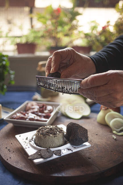 Cultiver un chef méconnaissable saupoudrer de fromage à pâte molle avec de la truffe à l'aide d'une râpe pendant la cuisson à table à la maison — Photo de stock