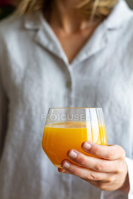 Colheita fêmea anônima em pé com copo de suco de laranja fresco para o café da manhã em casa — Fotografia de Stock