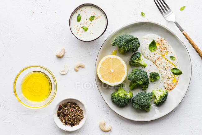 Вид зверху смачні брокколі зі свіжим лимоном та соусом біля мисок з оливковою олією та спеціями на столі — стокове фото