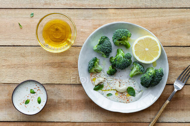 Vista dall'alto di gustosi broccoli con limone fresco e salsa vicino a ciotole con olio d'oliva e mix di spezie sul tavolo di legno — Foto stock