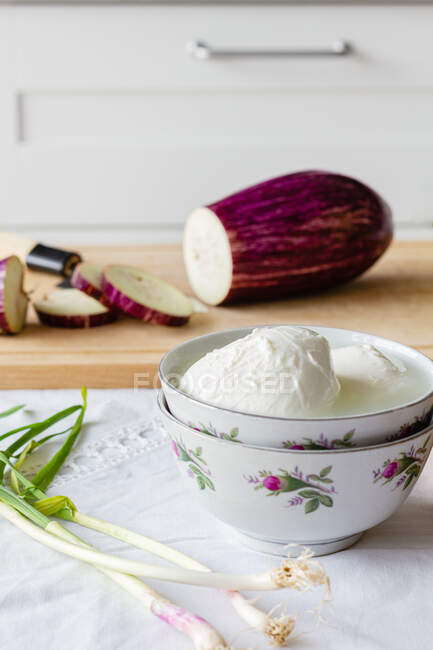 Bowl of mozzarella cheese with green onion and cut eggplant on chopping board for healthy lunch — Stock Photo