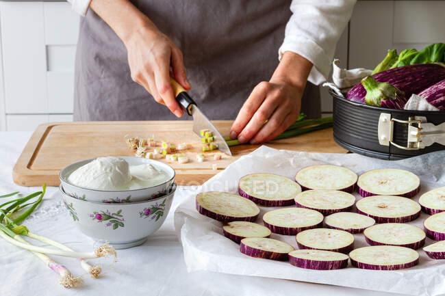 Crop anonymen Koch hacken grüne Zwiebeln, während die Vorspeise mit Auberginen und Käse in der Küche — Stockfoto