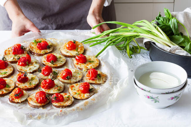 High angle of crop anonymous cook standing at table with plate of homemade baked appetizers made of eggplant mozzarella and cherry tomatoes with onion — Stock Photo