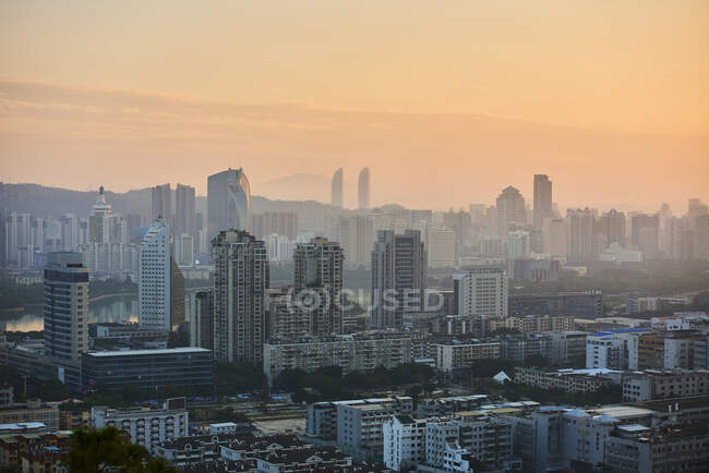 Мирний вид на сучасний мегаполіс з хмарочосами та житловими будівлями під оранжевим небом у сутінках — стокове фото