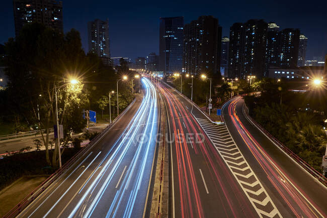 Longue exposition route asphaltée achalandée avec des véhicules de conduite dans la métropole urbaine contemporaine la nuit — Photo de stock