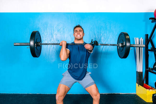 Atleta masculino poderoso sem gritos de mão enquanto levanta peso pesado durante o treinamento funcional perto de equipamentos esportivos no ginásio — Fotografia de Stock