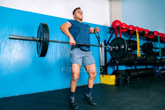 Мощный спортсмен без ручного подъема тяжелого веса во время функциональной тренировки возле спортивного инвентаря в спортзале — стоковое фото