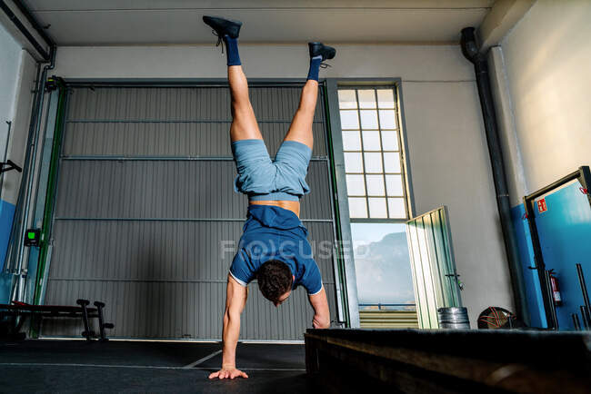 Back view of anonymous disabled male athlete in sportswear standing on hands during functional training in gymnasium — Stock Photo