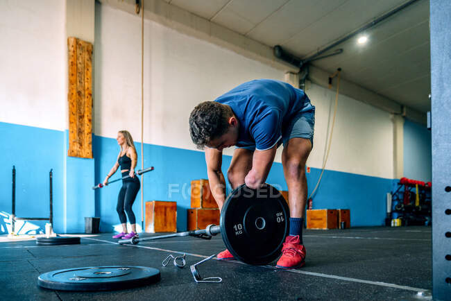Disabled male athlete leaning forward while putting plate on bar near sportswoman working out in gym — Stock Photo