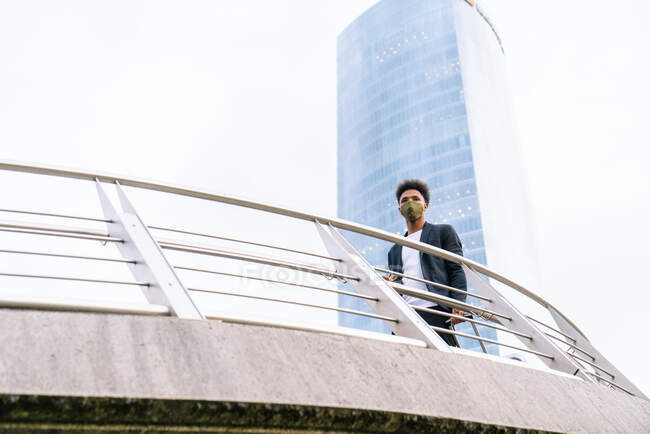 De baixo de confiante afro-americano masculino inclinado sobre trilhos enquanto de pé no centro da cidade e olhando para longe — Fotografia de Stock