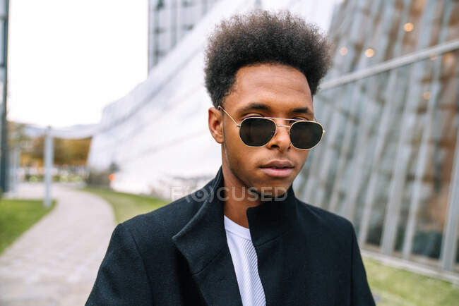 Homem afro-americano confiante em óculos de sol da moda e com penteado afro em pé na cidade e olhando para a câmera — Fotografia de Stock