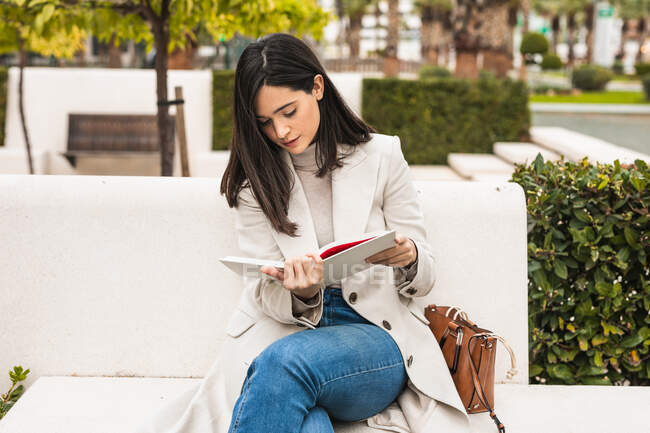 Жінка-підприємець сидить на лавці в парку і перевіряє розклад в блокноті — стокове фото