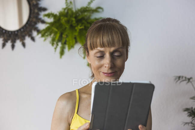Femme adulte souriante en tenue décontractée regardant la vidéo sur tablette moderne dans le salon léger — Photo de stock