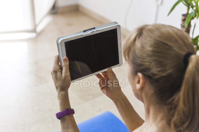 Доросла жінка в повсякденному одязі дивитися відео на сучасному планшеті у світлій вітальні — стокове фото