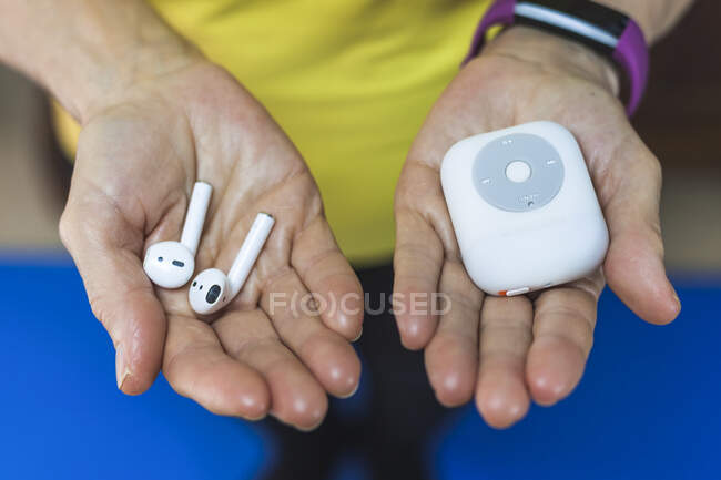 From above crop unrecognizable person wearing fitness bracelet showing wireless earbuds and modern mp3 player on hands — Stock Photo