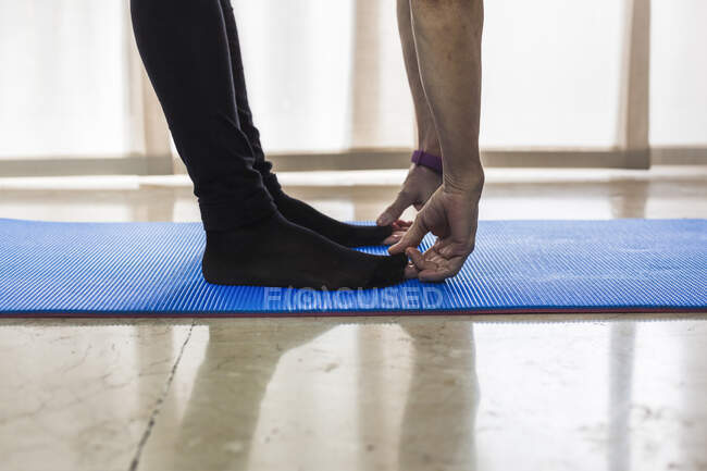 Side view crop unrecognizable female in leggings bending down and touching tips while stretching body on blue mat in light studio — Stock Photo