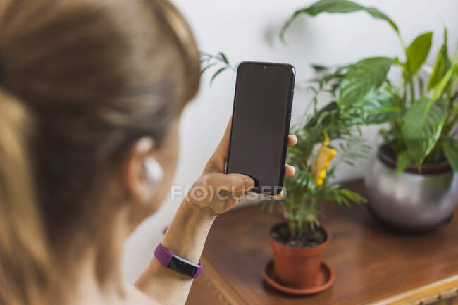 Vista posteriore femmina adulta in auricolari con videochiamata attraverso il moderno telefono cellulare in soggiorno leggero — Foto stock