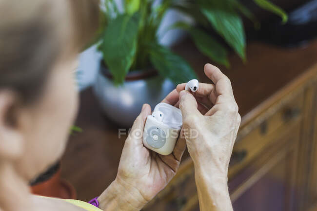 From above crop unrecognizable person wearing fitness bracelet showing wireless earbuds and modern mp3 player on hands — Stock Photo