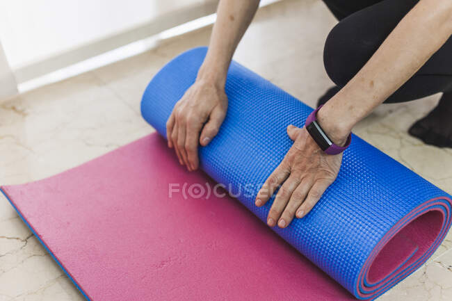 Vista laterale adulto donna in abbigliamento sportivo rolling yoga mat dopo un intenso allenamento nel centro fitness leggero — Foto stock