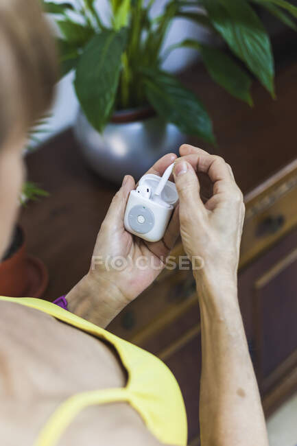 De arriba recorte irreconocible persona que usa pulsera de fitness que muestra auriculares inalámbricos y reproductor de mp3 moderno en las manos - foto de stock