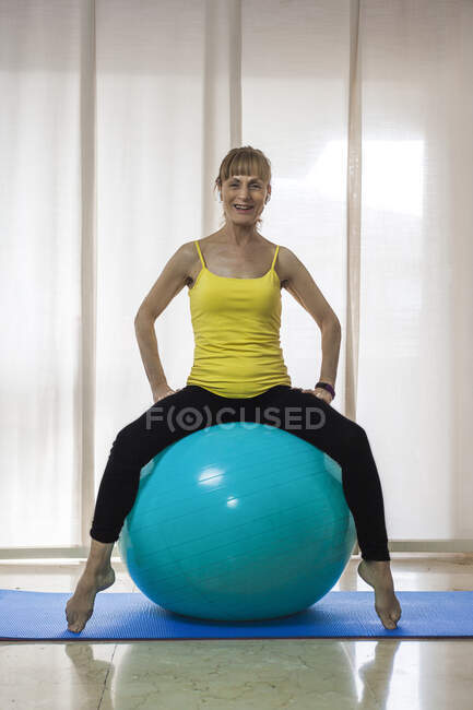 Fit femelle en vêtements de sport assis sur une grosse balle de yoga dans un centre de fitness léger et regardant la caméra — Photo de stock