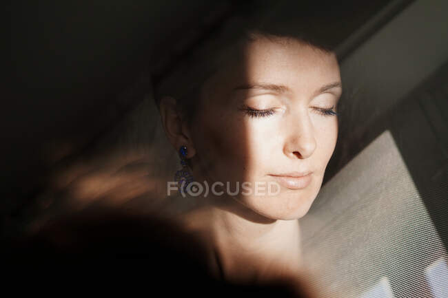 Through glass of peaceful adult lady with short hair recreating with closed eyes on sunny day — Stock Photo