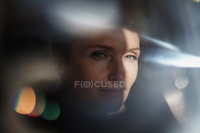 Through glass of peaceful adult lady with short hair looking at camera on sunny day — Stock Photo