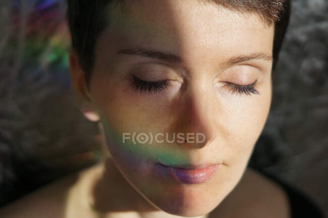 Crop feminine thoughtful adult lady with natural makeup and short hair smiling with eyes closed dreamily in sunlight — Stock Photo
