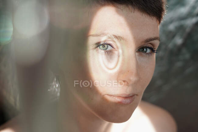 Através de vidro de senhora adulta pacífica com cabelo curto olhando para a câmera no dia ensolarado — Fotografia de Stock