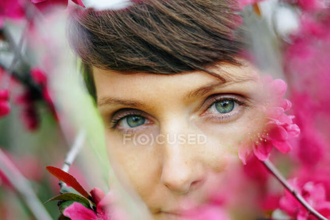 Nachdenkliches Weibchen mit kurzen Haaren, das sich im grünen Garten in der Nähe hell blühender Blumen erholt und in die Kamera blickt — Stockfoto