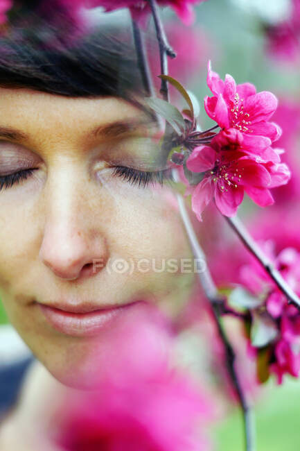 Задумчивый урожай взрослой женщины с короткими волосами воссоздания в зеленом саду рядом с яркими цветущими цветами с закрытыми глазами — стоковое фото