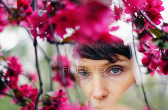 Crop pensive adult female with short hair recreating in green garden near bright blossoming flowers and looking at camera — Stock Photo
