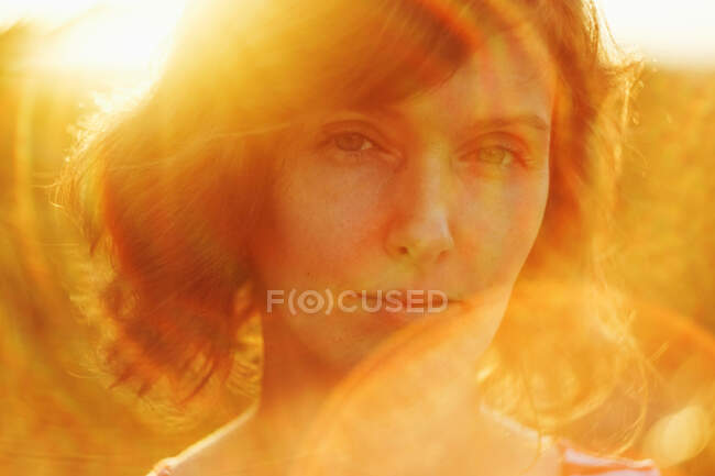 Задумчивая взрослая женщина, отдыхающая на природе и задумчиво смотрящая в камеру под ярким солнечным светом в золотой час — стоковое фото
