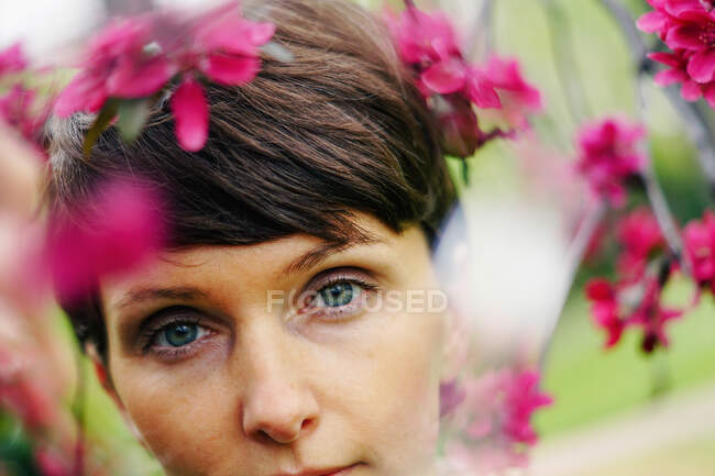 Nachdenkliches Weibchen mit kurzen Haaren, das sich im grünen Garten in der Nähe hell blühender Blumen erholt und in die Kamera blickt — Stockfoto