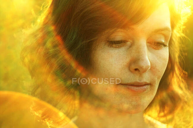 Crop thoughtful adult female resting in nature and looking down pensively under bright sunlight during golden hour — Stock Photo