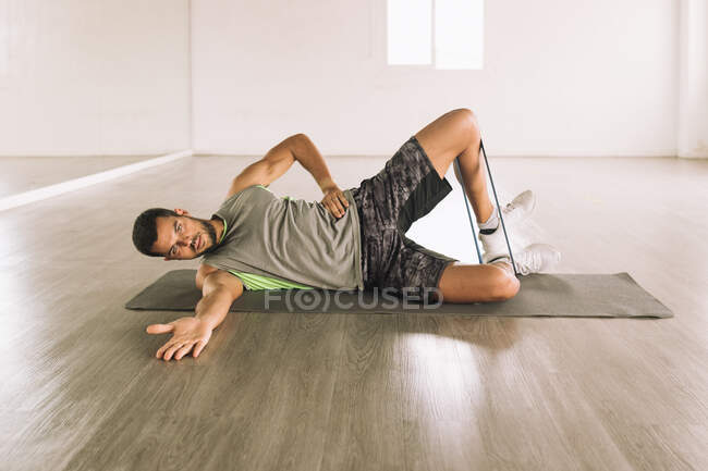 Cuerpo completo de joven deportista determinado en forma enfocada en ropa deportiva realizando High Side Plank con pierna levanta ejercicio durante el entrenamiento en estudio cerca de espejo de pared grande - foto de stock