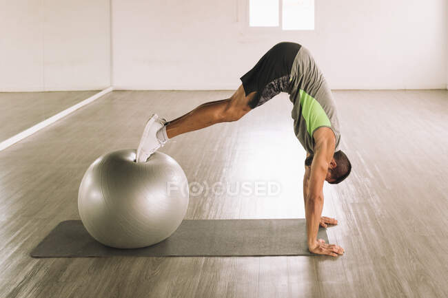 Vue latérale d'un jeune athlète masculin musclé méconnaissable en tenue de sport effectuant un exercice Swiss Ball Pike sur tapis pendant l'entraînement en studio — Photo de stock