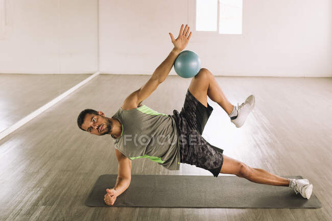 Вид сбоку решительного мускулистого молодого человека в спортивной одежде, выполняющего упражнение 